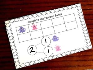 Number bonds with monsters worksheet on a wooden background. 