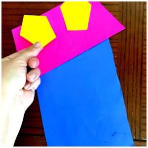 Adding yellow windows to a fraction craft house made of blue and pink construction paper. 