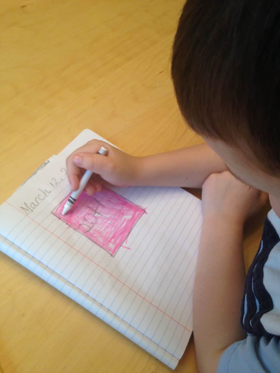 A child coloring a square pink on lined paper. 