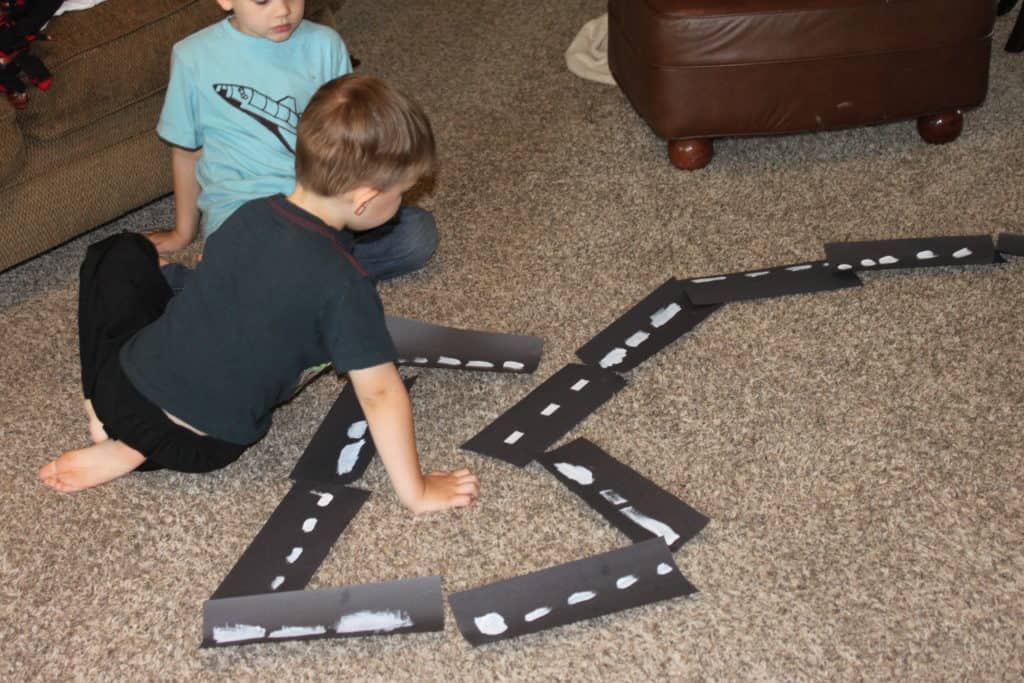 Children creating a race track using black construction paper. 