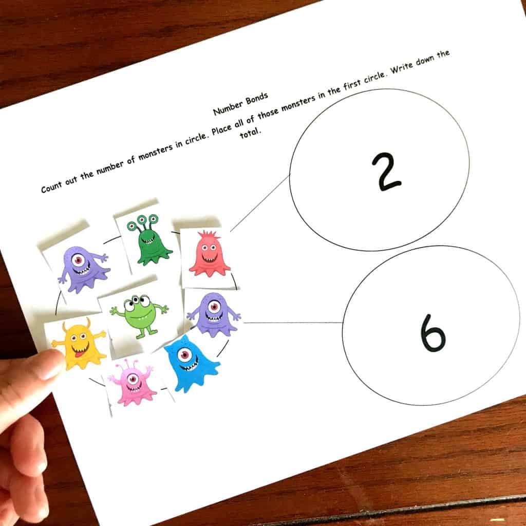 Preschool math worksheets with monsters to practice number bonds with a hand holding onto a picture of a yellow monster. 