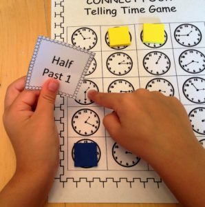 Time games using a bingo card with clocks showing various times with pieces of yellow paper covering them up.
