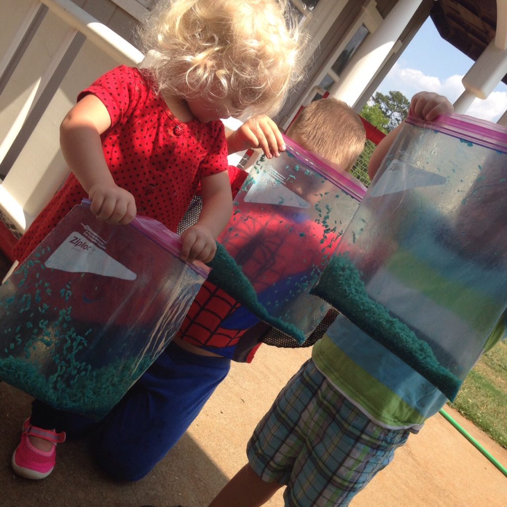 Three children holding bags of dyed blue rice for a sensory game. 