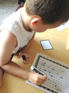 A child solving a number puzzle by using a blue marker to cross out numbers.  