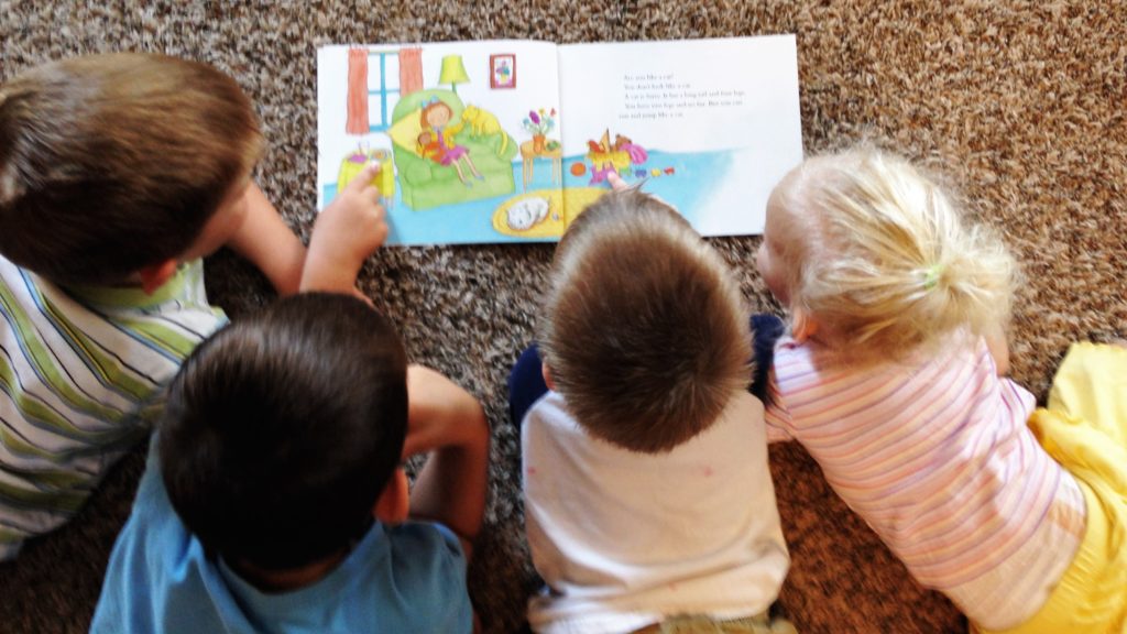 4 children laying on a carpet reading a book. 