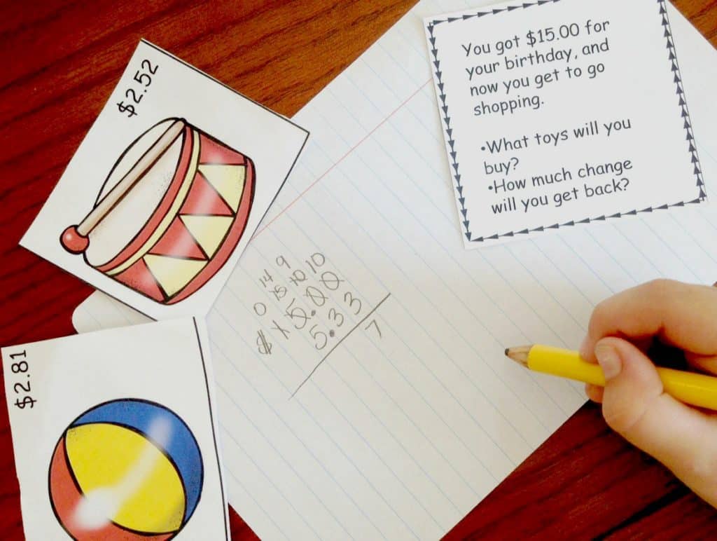 A child's hand is working on a making change math problem with pictures of objects and their prices. 