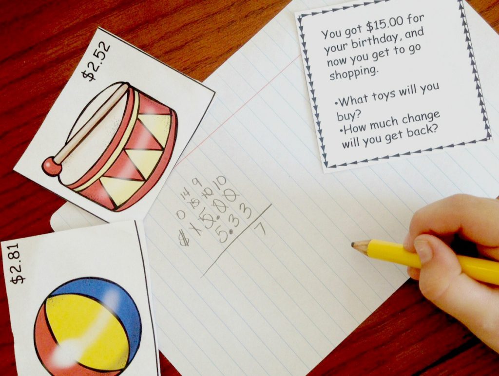 A child's hand is working on a making change math problem with pictures of objects and their prices. 