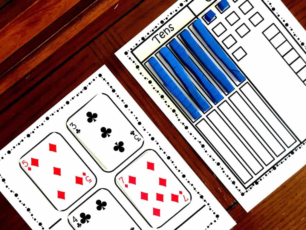 Subtraction regrouping game printable with game pieces and base ten blocks on a wooden table. 