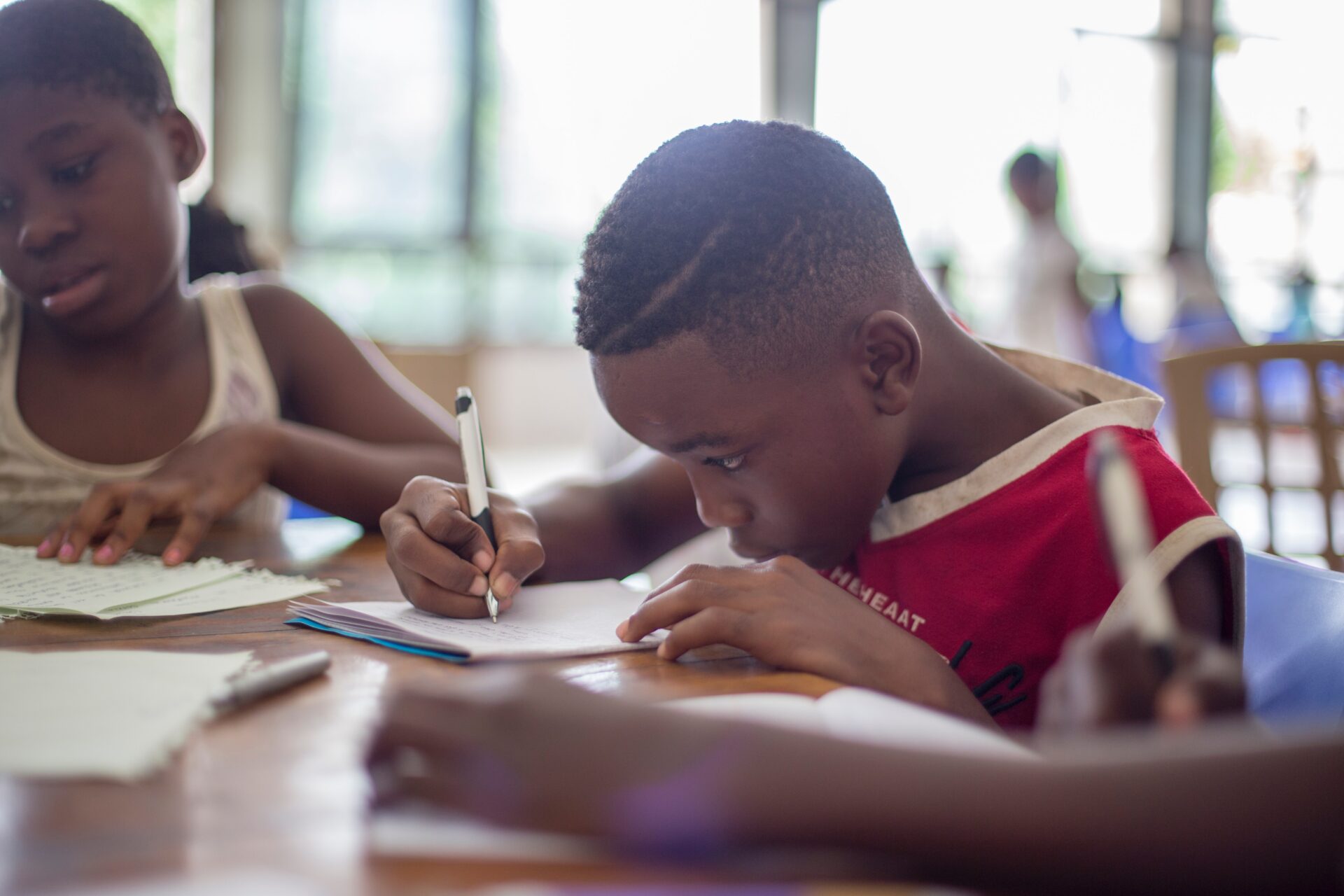 Little boy working on a math problem with a girl in the background.